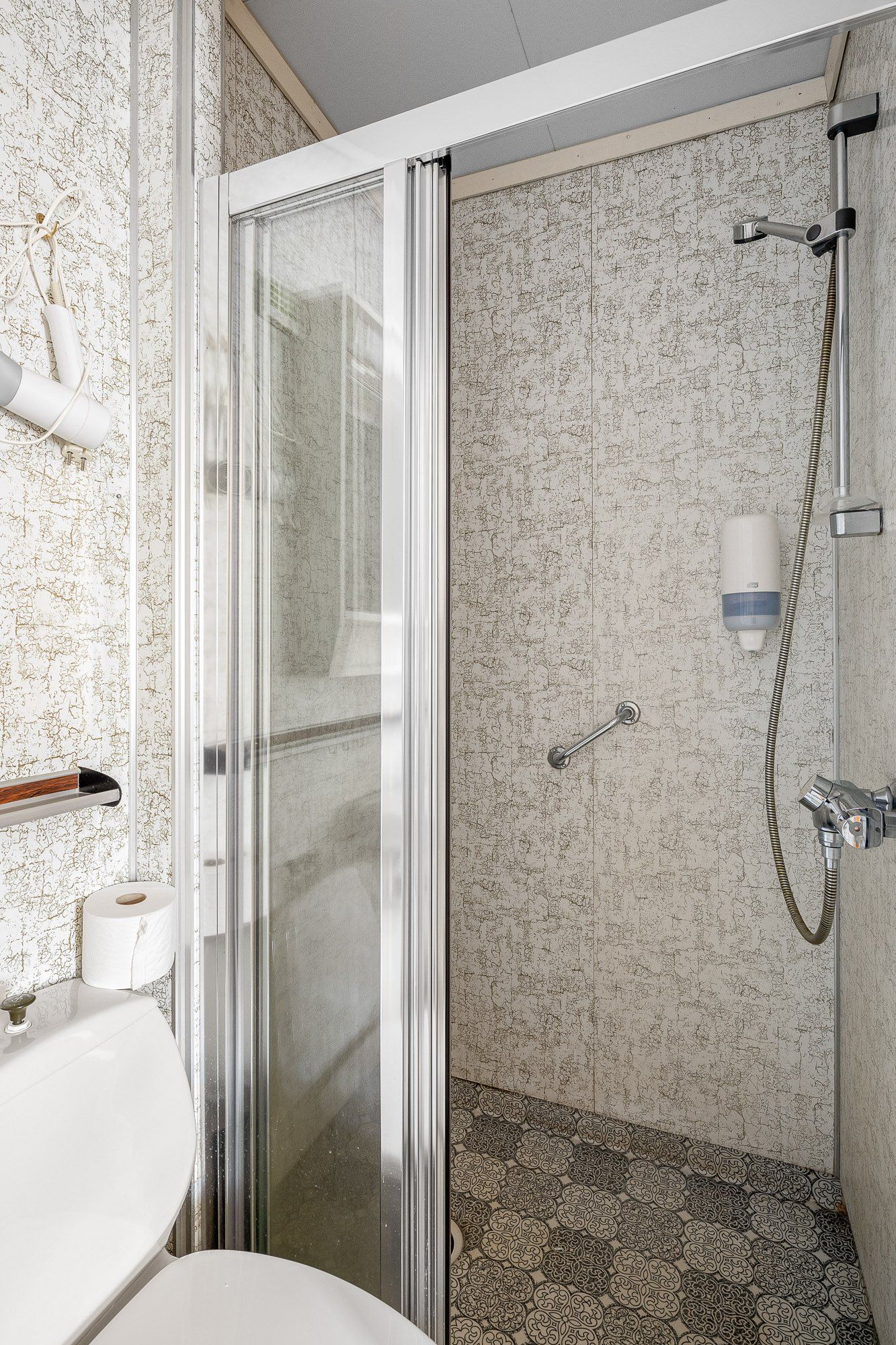 Small tiled shower stall with glass door, handheld showerhead, and built-in shelf in a bathroom.