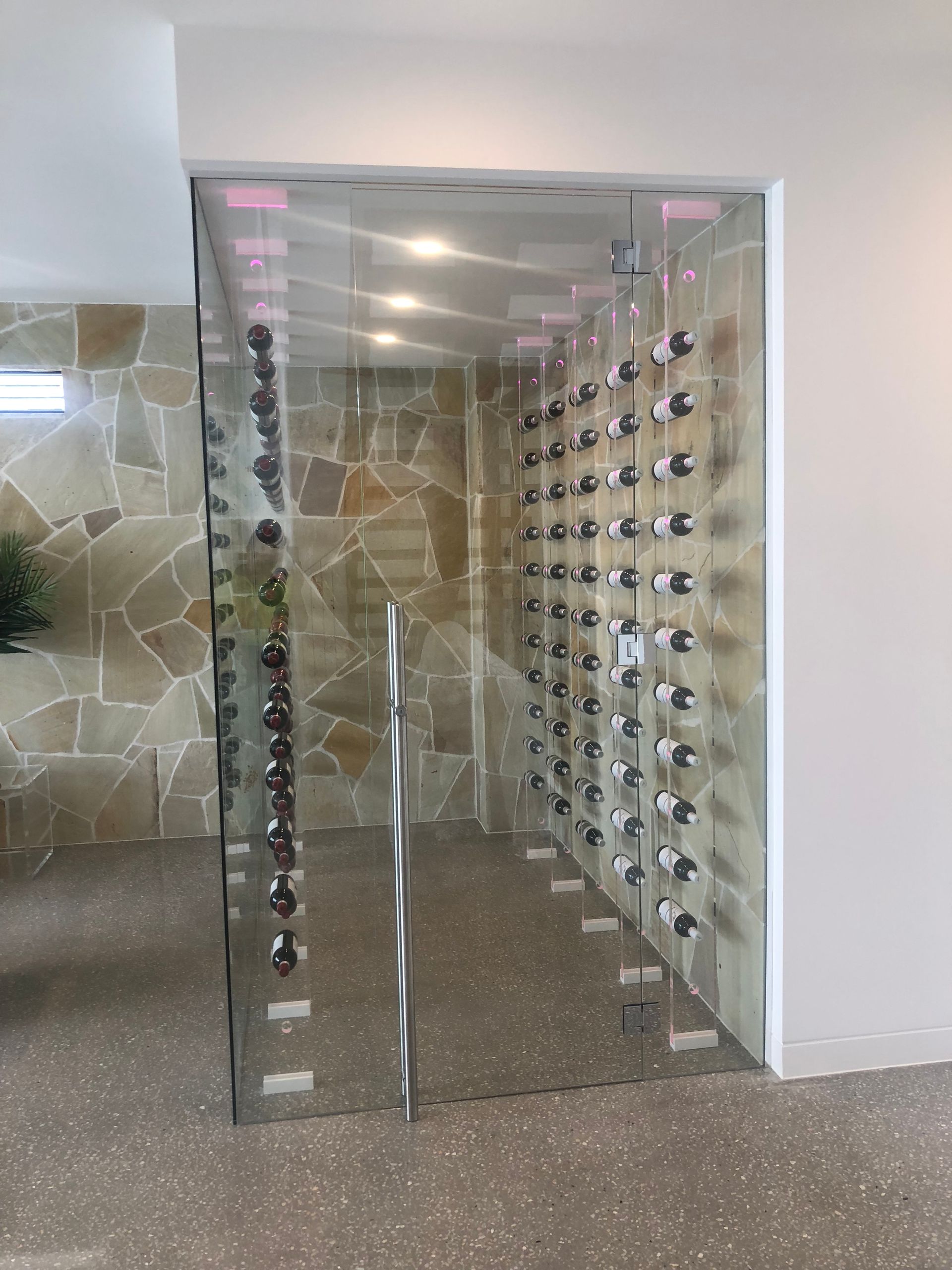 A glass door leading to a wine cellar filled with wine bottles.