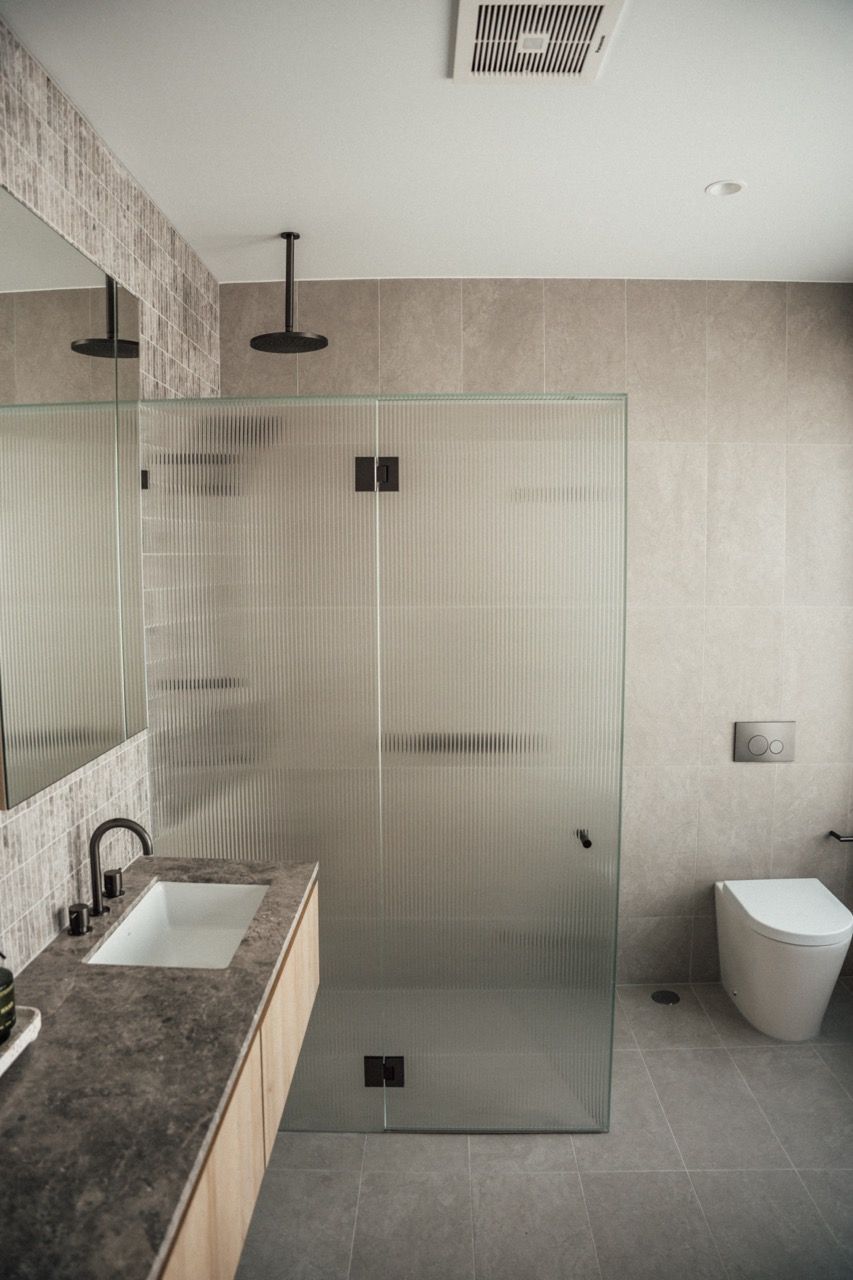 A bathroom with a walk in shower , toilet , sink and mirror.