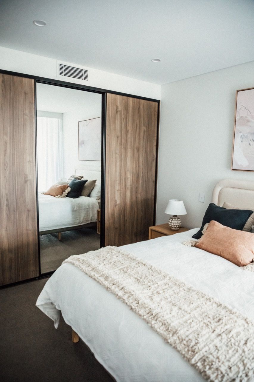 A bedroom with a bed , nightstands , a mirror and a brick wall.