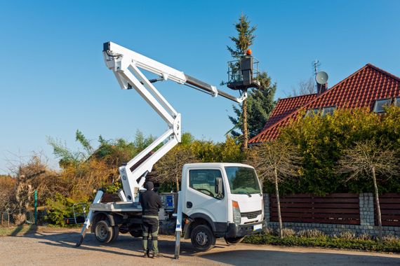 White utility truck with raised boom lift parked on a residential street beside houses and trees
