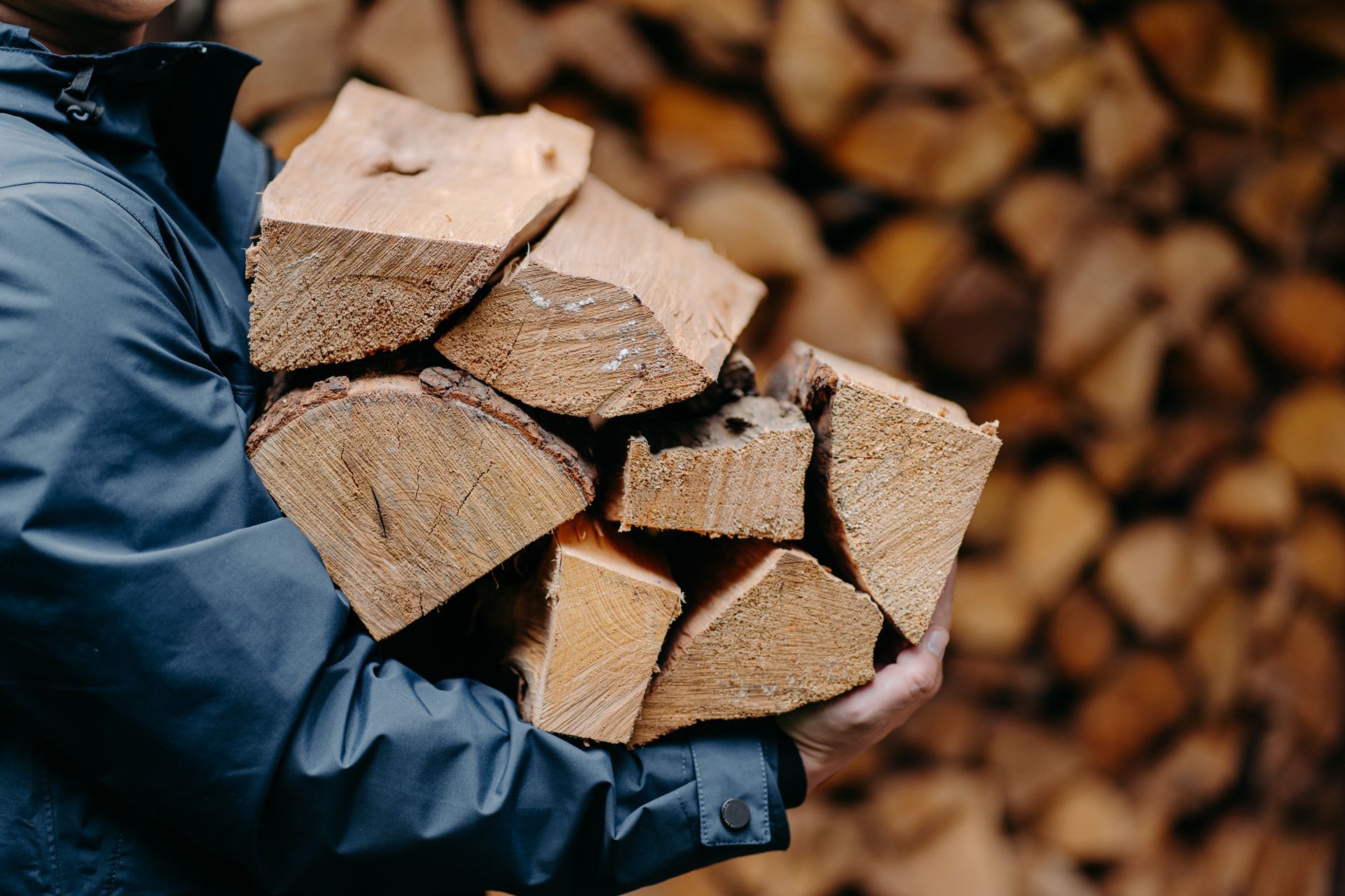 Gloved hands carrying chopped firewood logs with a blurred woodpile background