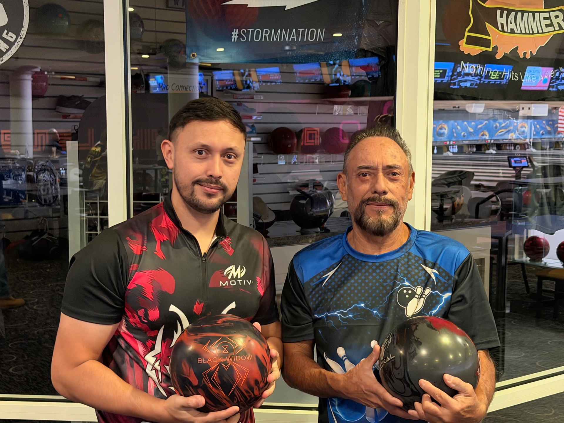 Two men in a bowling alley holding bowling balls, with arcade games in the background