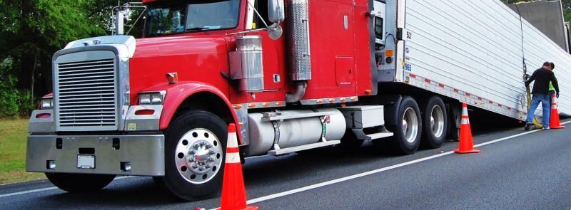 Red semi-truck parked on a roadside, with orange traffic cones beside the trailer.