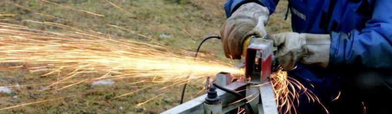 Worker using an angle grinder, throwing sparks while cutting metal outdoors