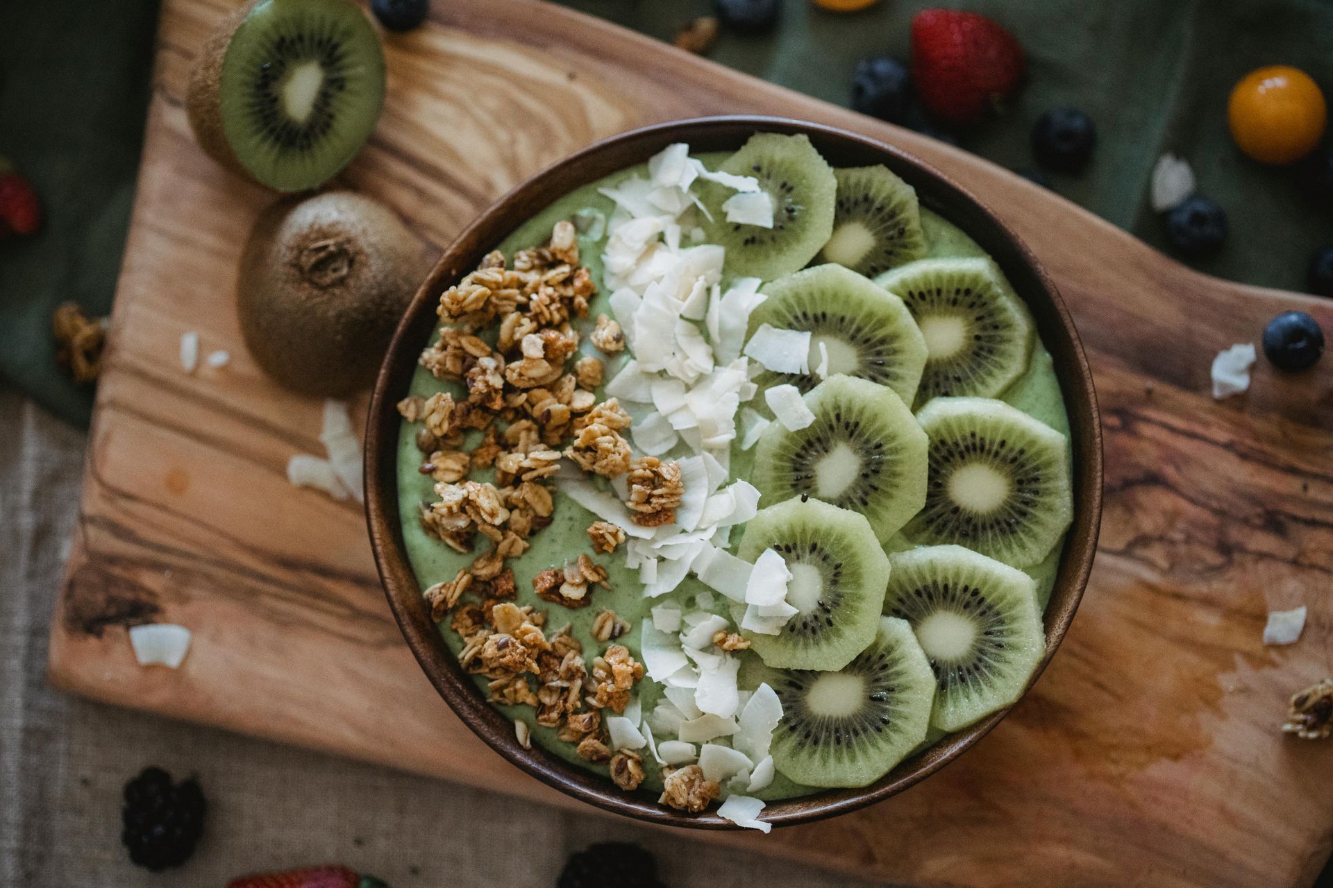 Green smoothie bowl with kiwi slices, granola, and coconut flakes on a wooden board — All Body Holistic Health in Thuringowa Central, QLD