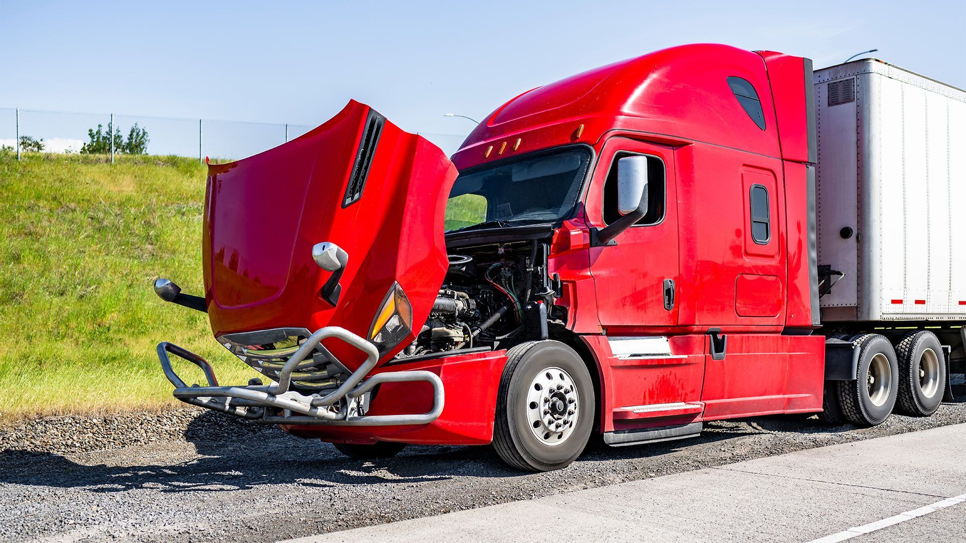 A red semi truck with its hood open is parked on the side of the road.