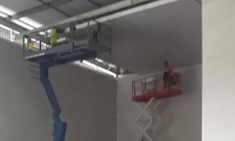 A man is standing on a scissor lift in a room.