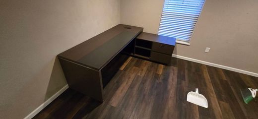 Empty room with a dark wood desk, small cabinet, wood floor, and a window with blinds.