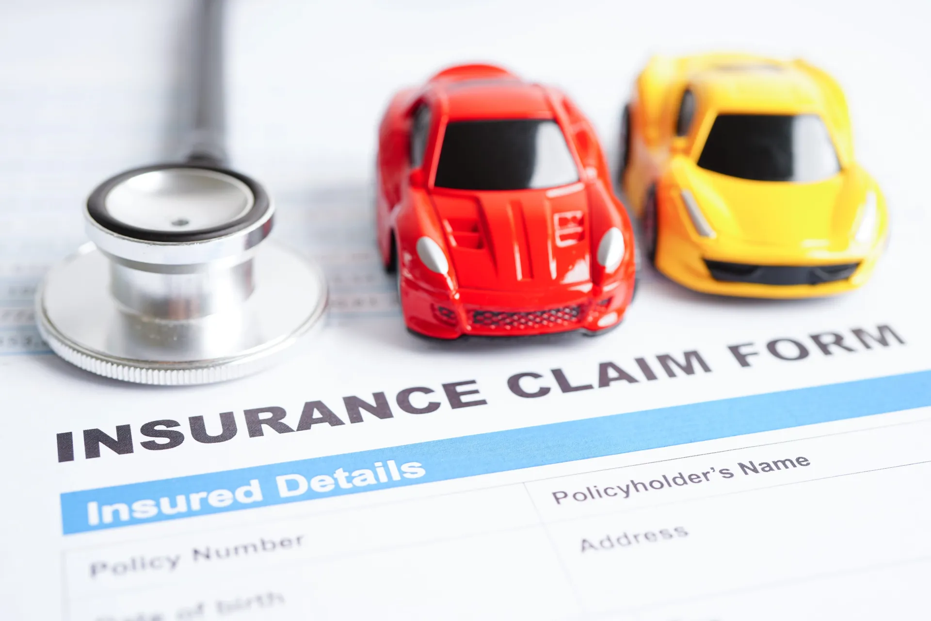 Insurance claim form with stethoscope and red and yellow toy cars