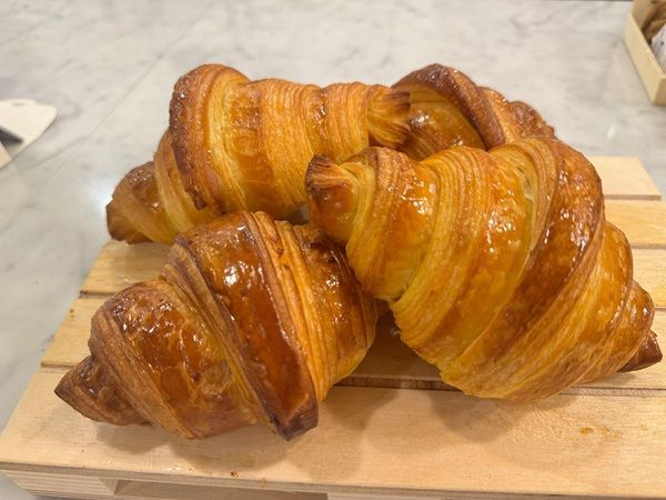 Due croissant dorati su un tagliere di legno, con strati sfogliati e crosta lucida.