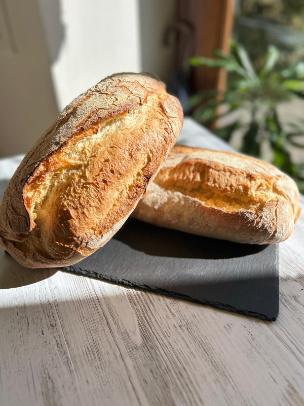 Due baguette croccanti su un tagliere scuro alla luce del sole su un tavolo di legno chiaro