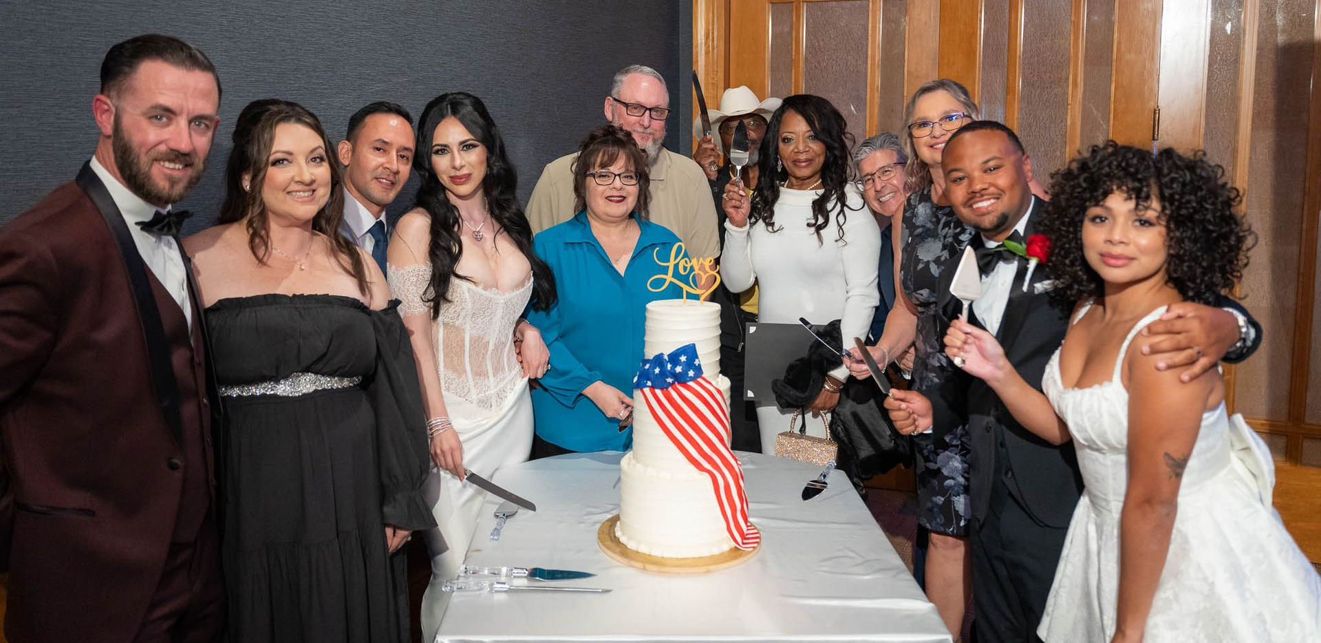 Group of people celebrate at a party, gathered around a cake with an American flag.