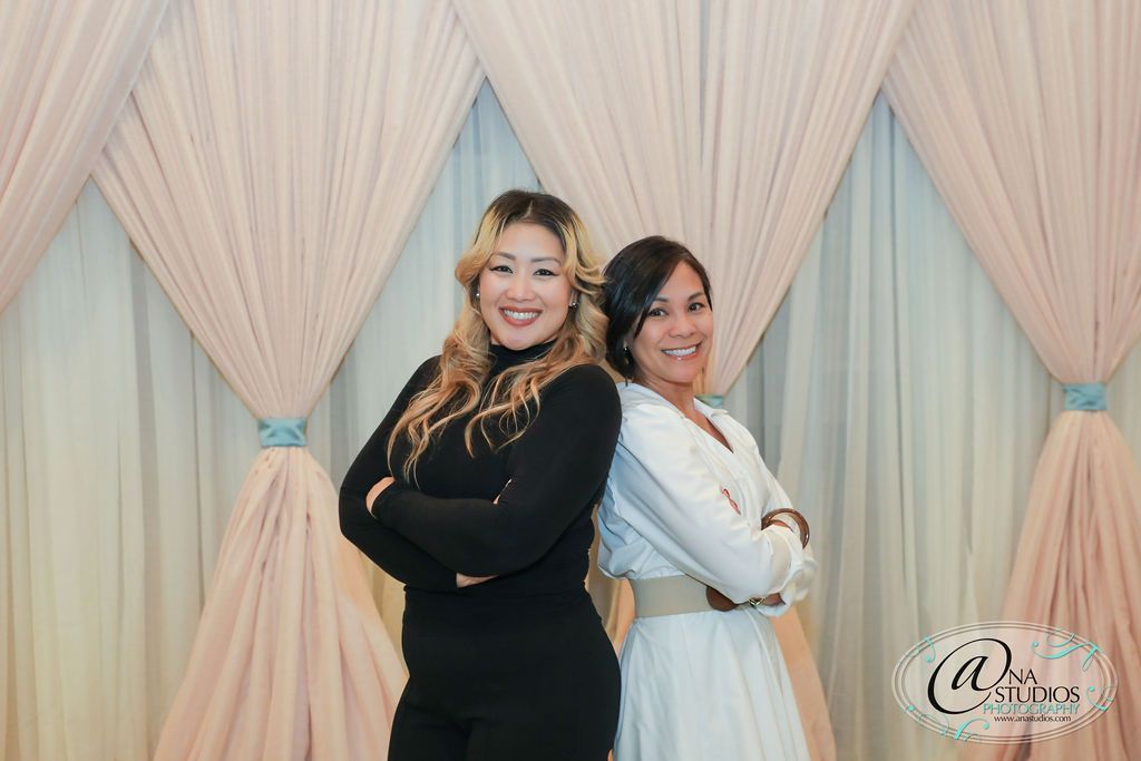 Two women are posing for a picture in front of a pink curtain.