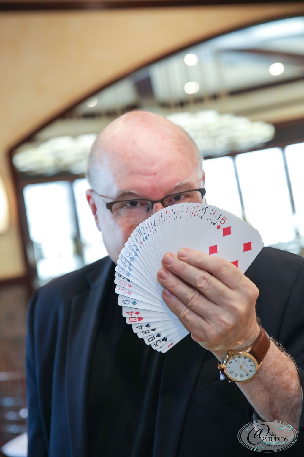 A man in a suit is holding a fan of playing cards in front of his face.