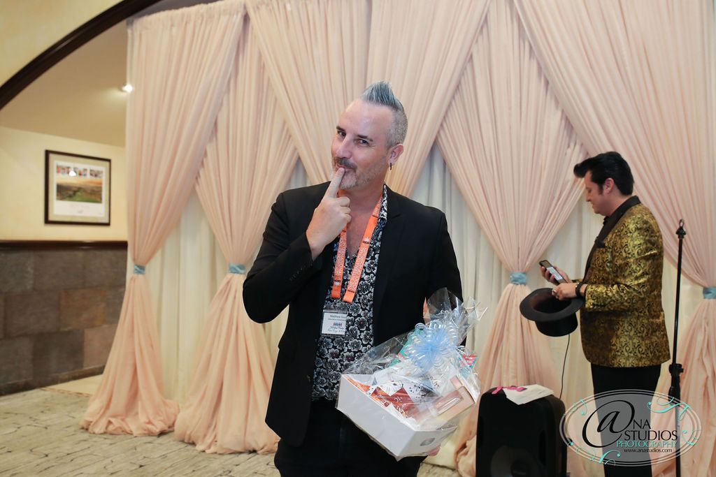 A man in a suit is standing in front of a microphone holding a gift box.