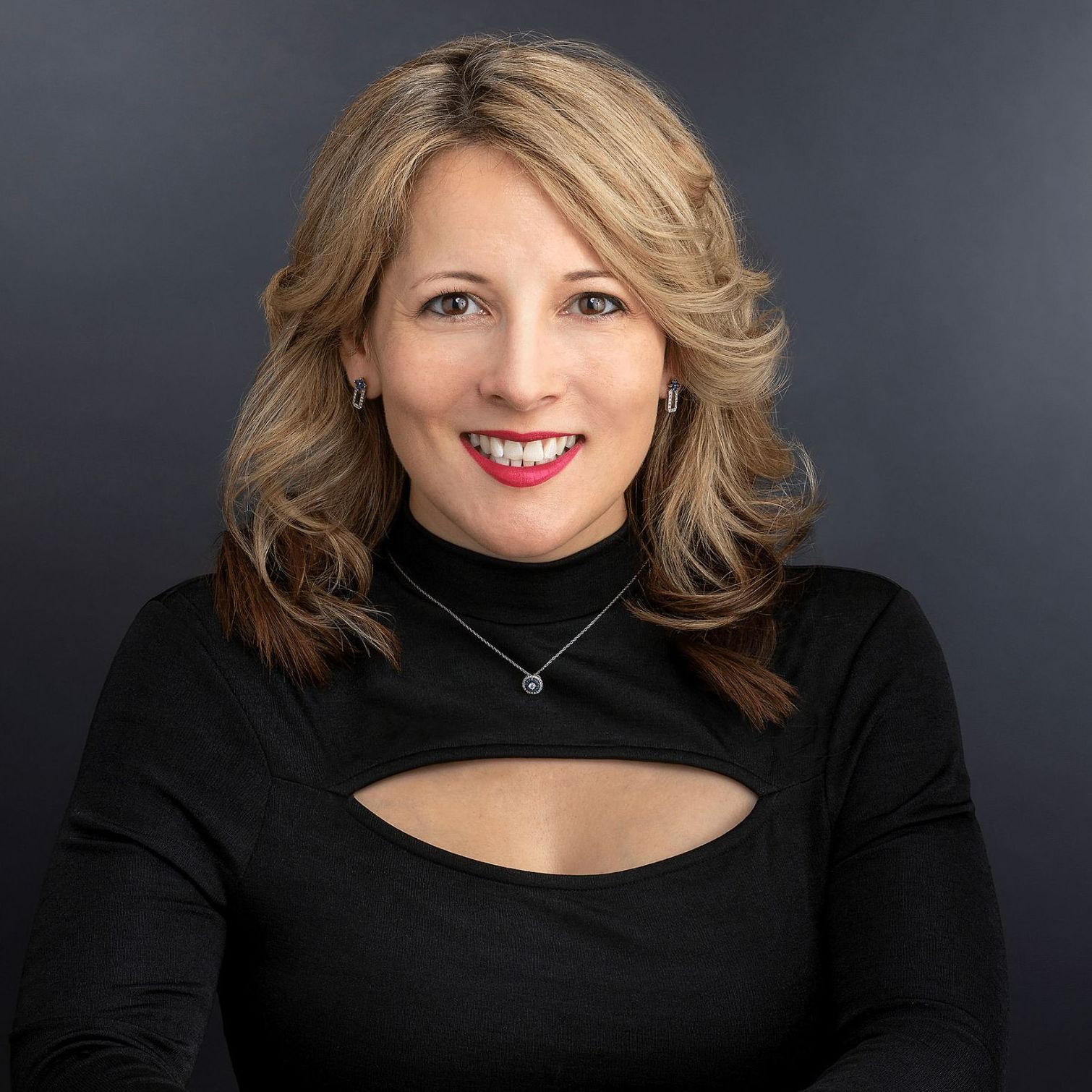 A woman wearing a black top and a necklace is smiling for the camera.