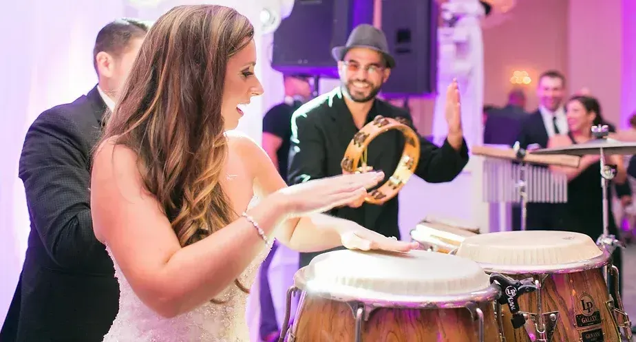 A bride and groom are playing drums at their wedding reception.