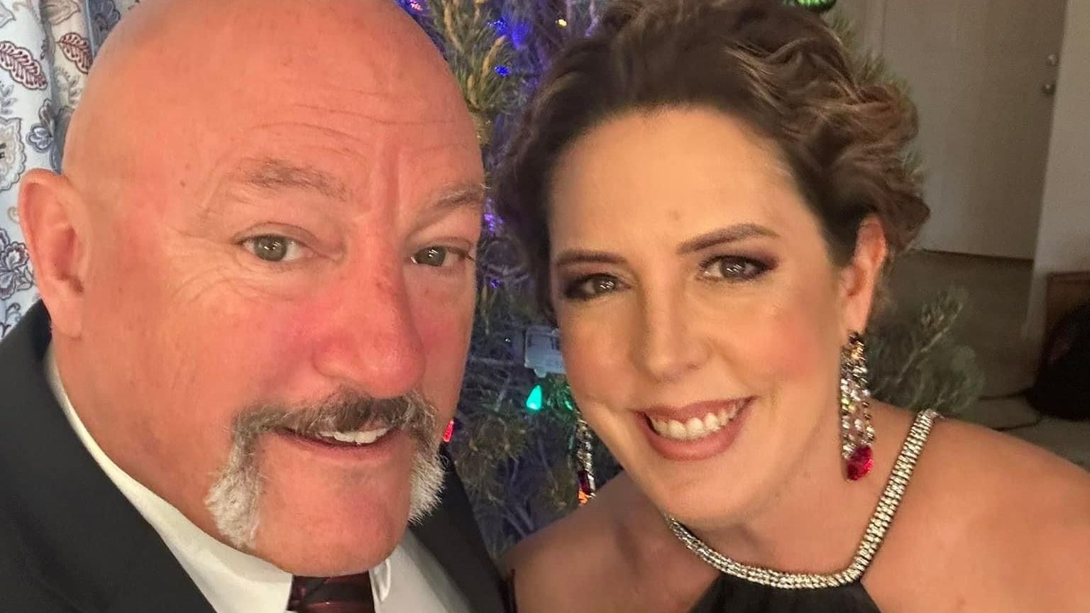 A man and a woman are posing for a picture in front of a christmas tree.