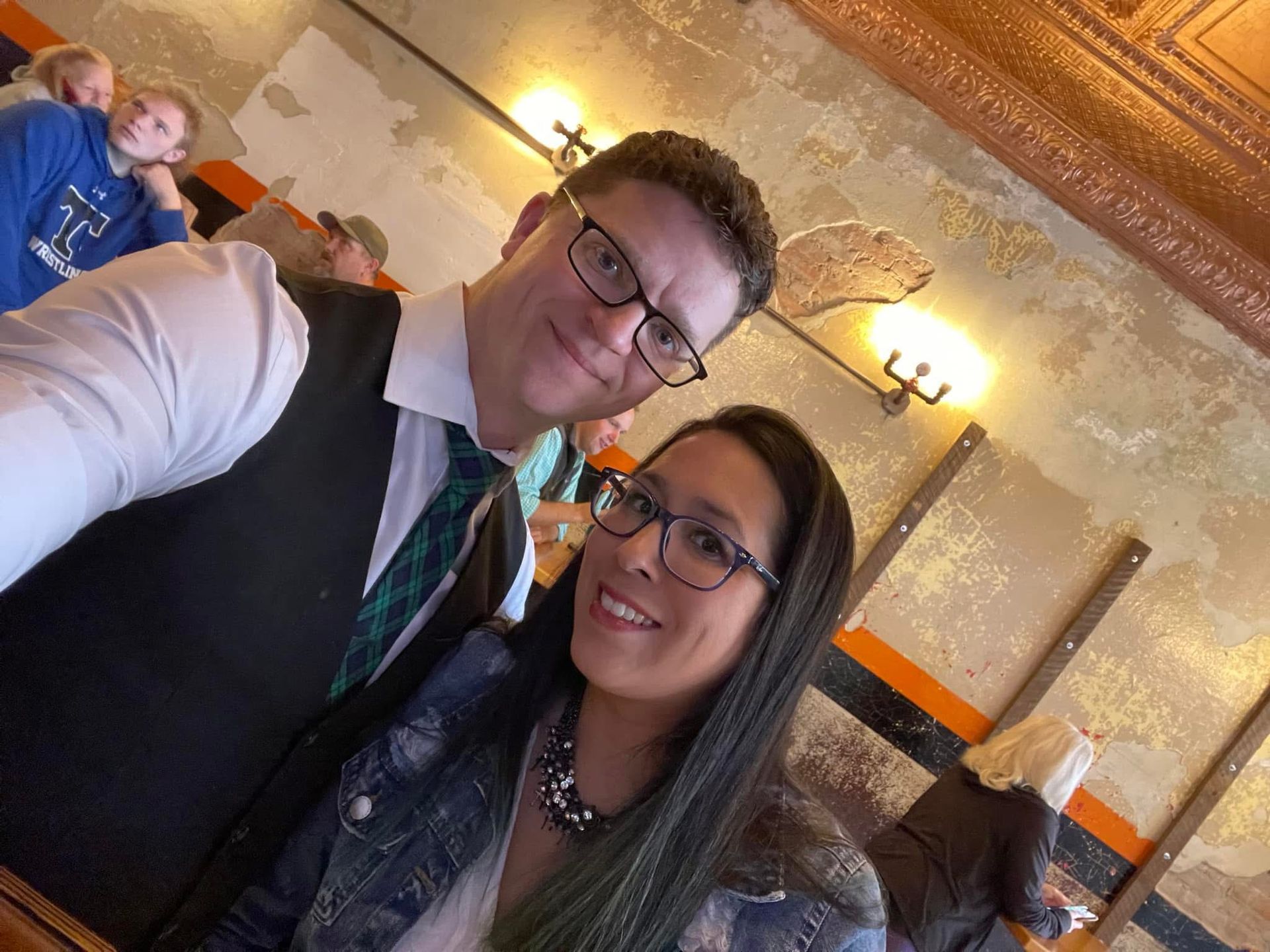 Two people posing for a selfie in a warmly lit ornate room with gold ceilings and wall sconces