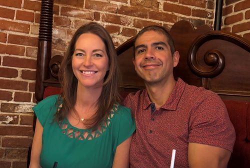 Two people smiling at a restaurant table with a brick wall backdrop
