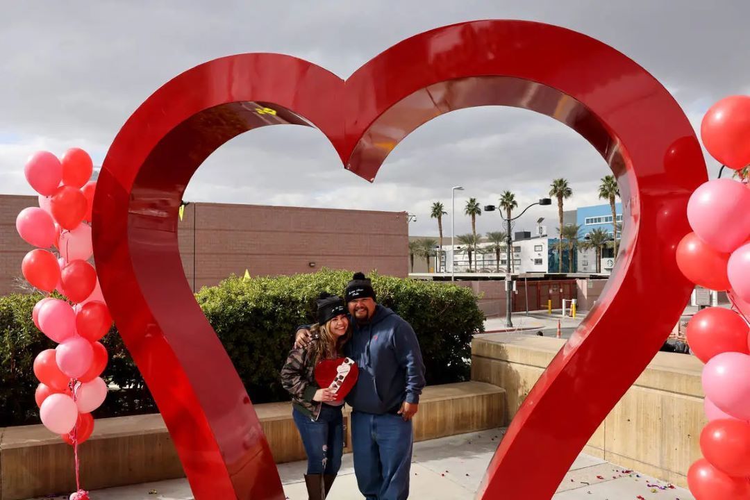 A man and a woman are standing in front of a large red heart.
