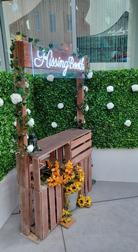 A wooden bench with flowers and a sign in front of a green wall.