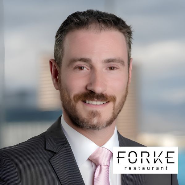 Portrait of a smiling man in a suit with a pink tie, beside the Forke restaurant logo