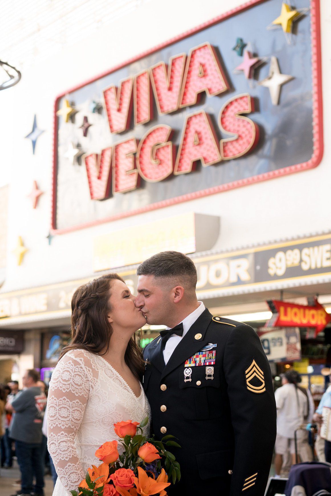 A bride and groom kissing in front of a viva vegas sign.