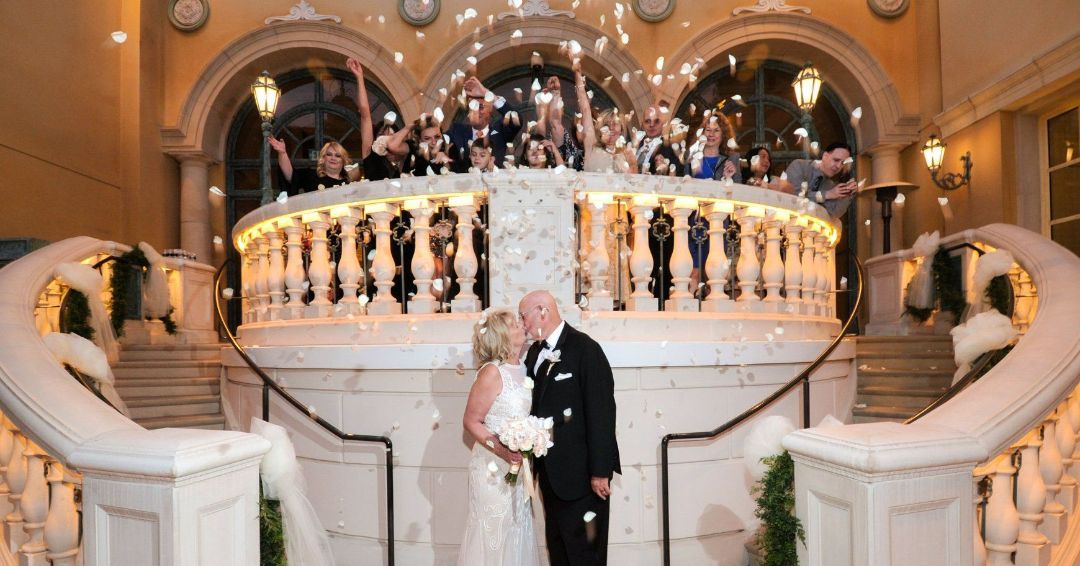 A bride and groom are kissing on a balcony at their wedding reception.