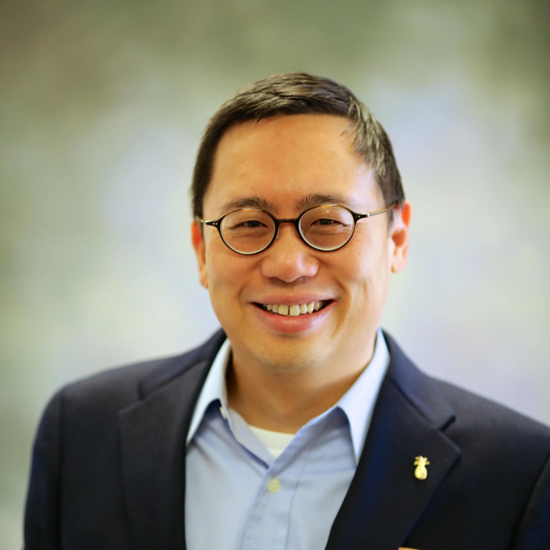 A man wearing glasses and a suit smiles for the camera