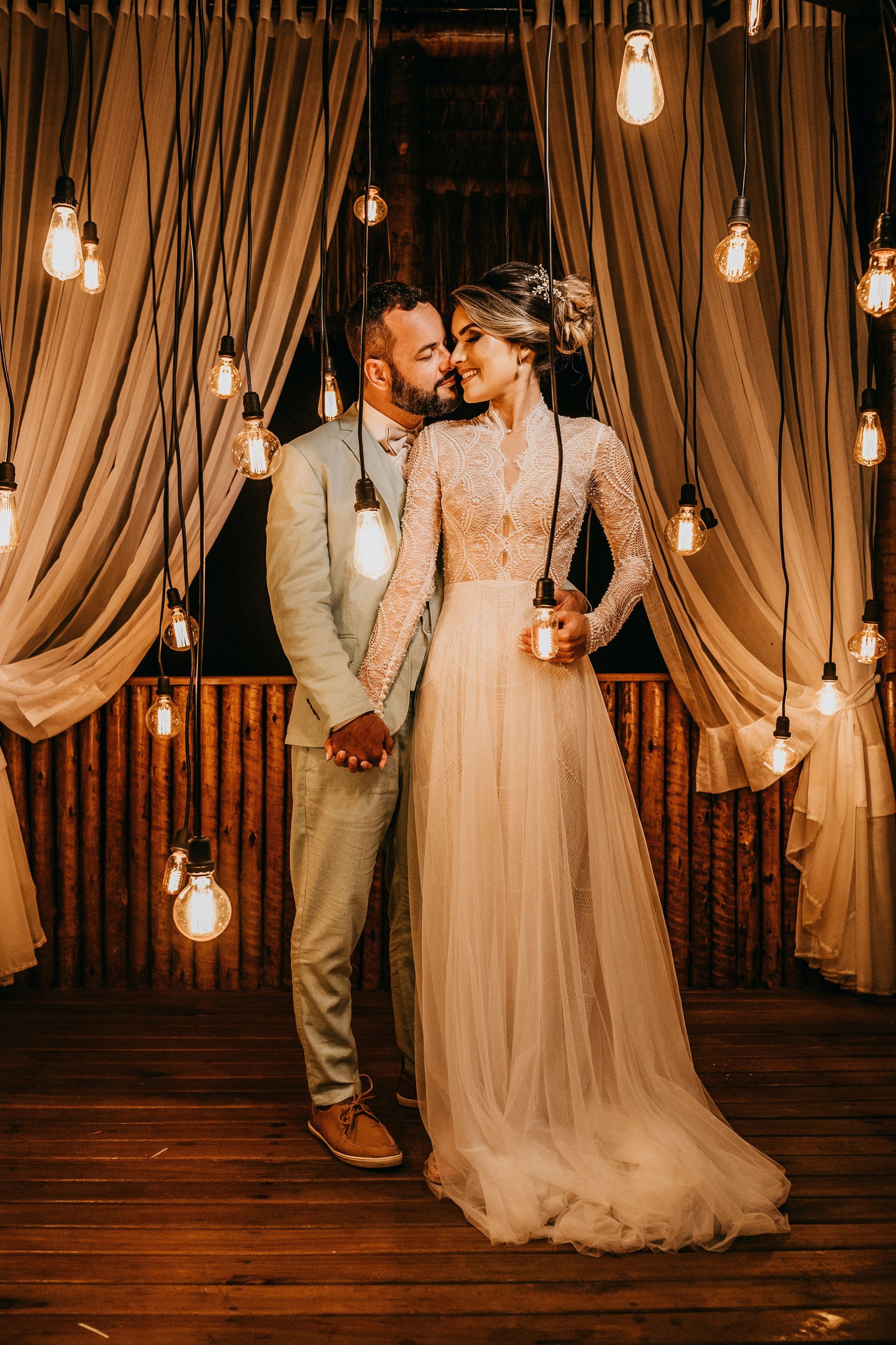 A bride and groom are posing for a picture in front of a string of lights.
