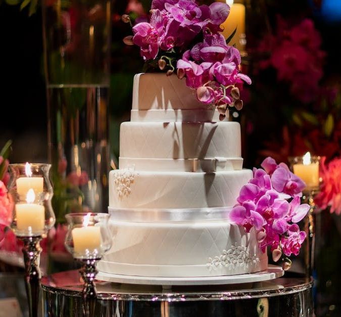 A wedding cake with purple flowers and candles on a table