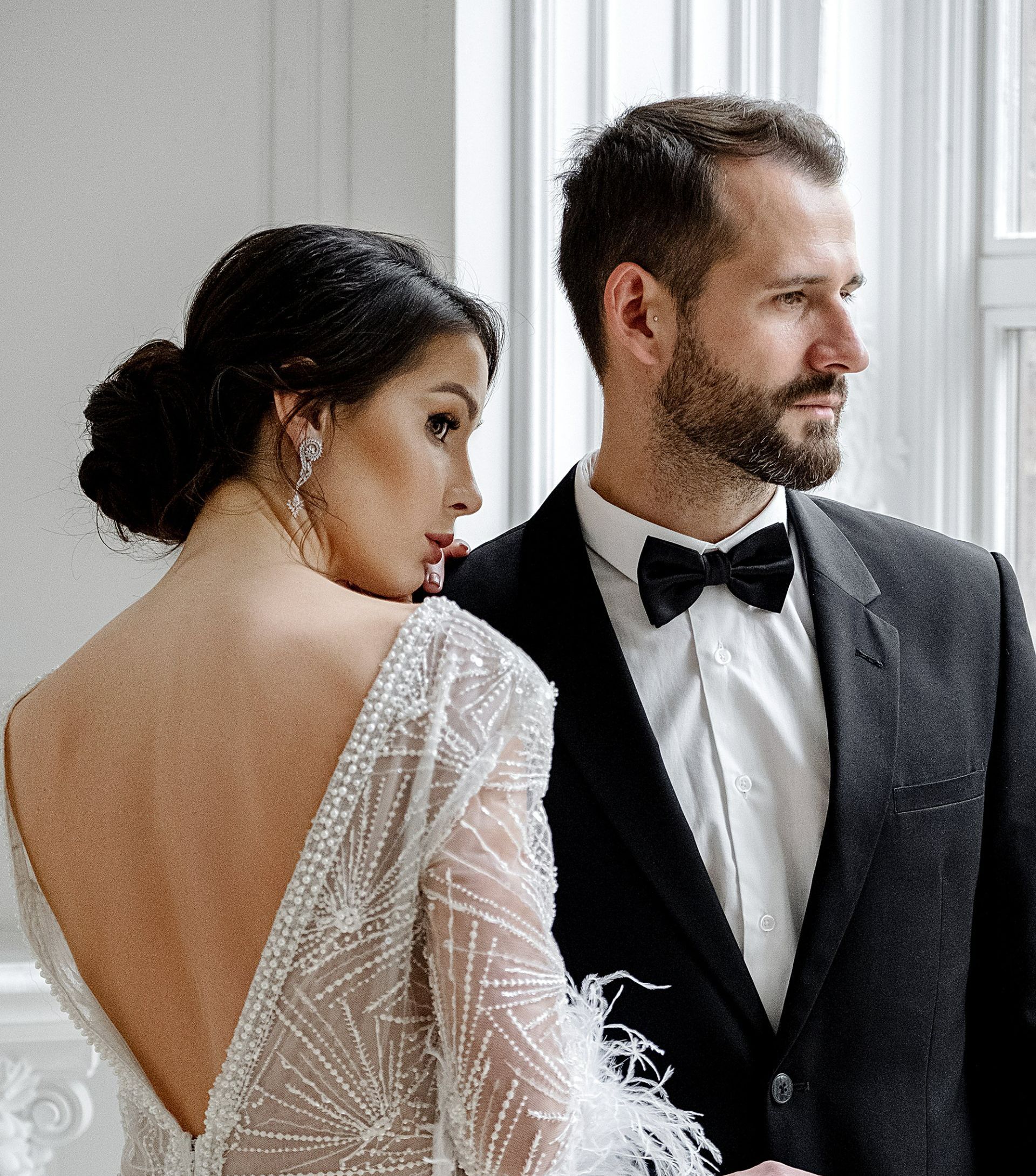 A bride and groom are standing next to each other in front of a window.