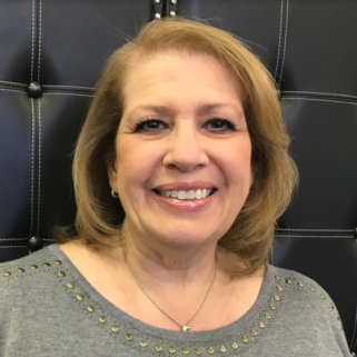 A woman wearing a gray shirt and a necklace is smiling for the camera.