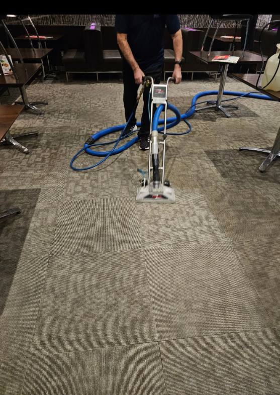 Person using a carpet cleaner in a carpeted room with chairs and tables nearby