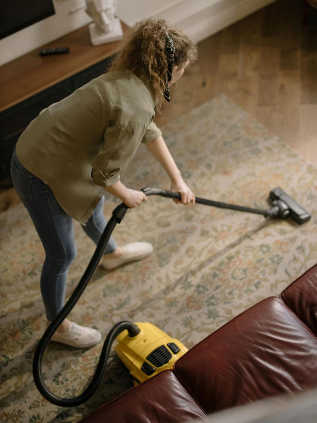 Person vacuuming a rug in a living room with a yellow canister vacuum