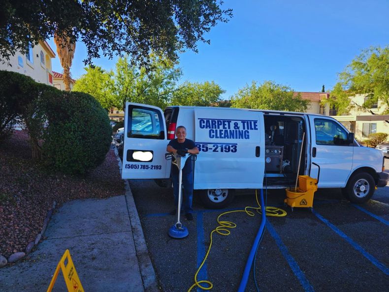 White cleaning van with open side door and carpet-cleaning equipment on a sunny driveway