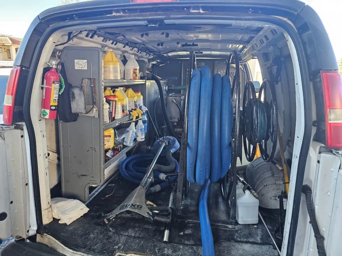 Van with open rear doors showing organized cleaning equipment, hoses, and supplies inside an industrial setup