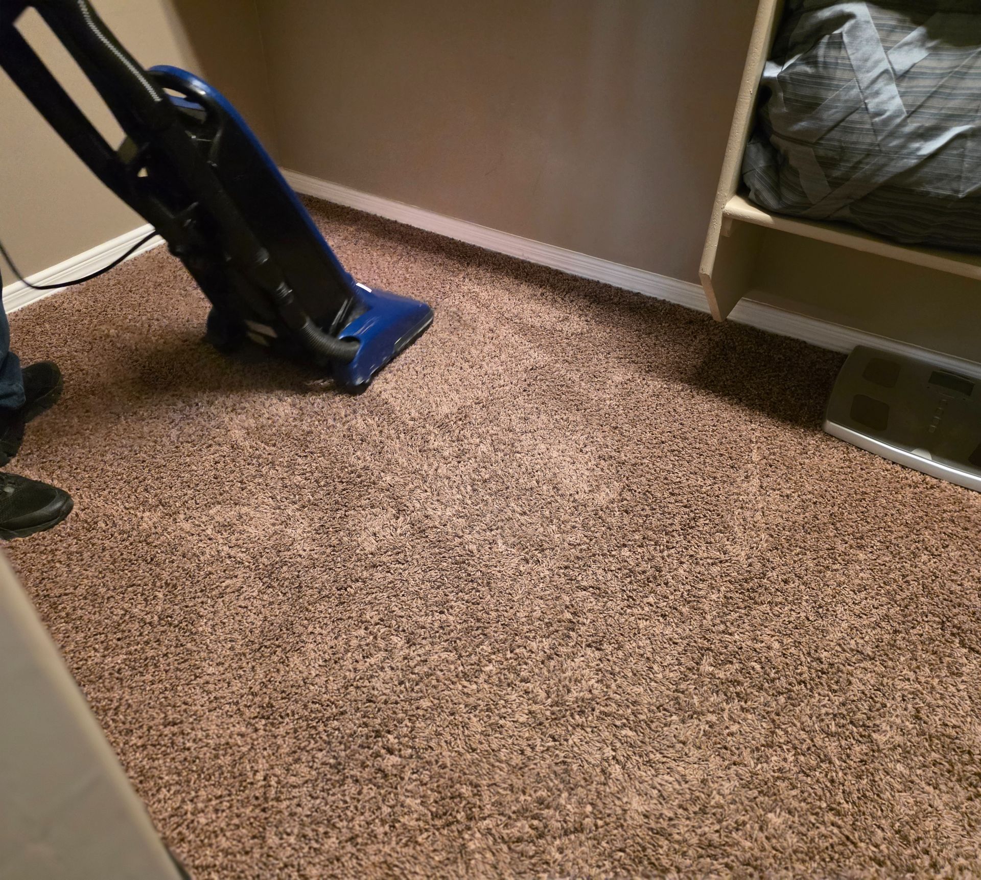 Blue upright vacuum on beige carpet in a corner of a room
