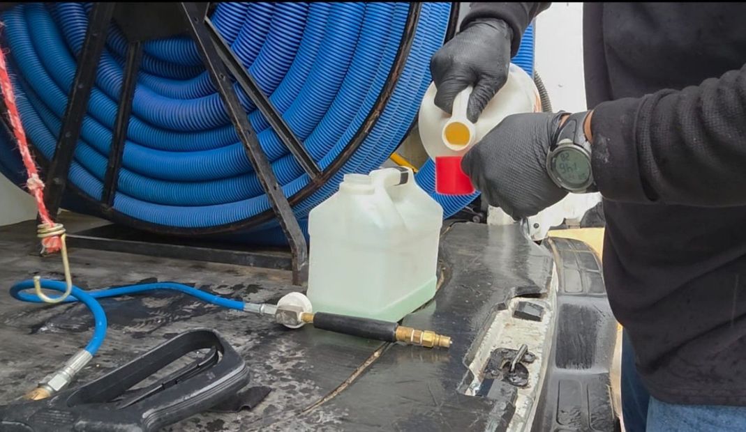 Gloved worker pours liquid into a plastic jug on a boat deck with coiled blue hoses in the background