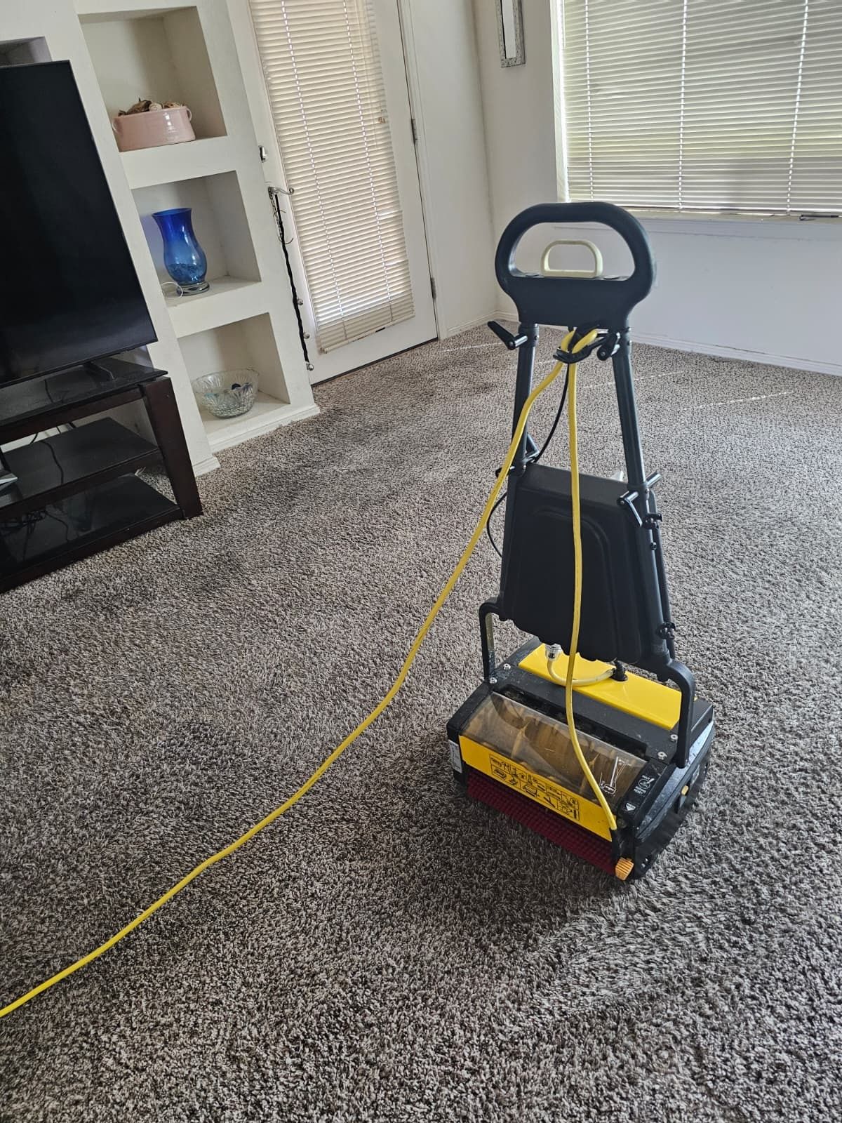 Yellow vacuum cleaner on a carpeted living room floor, with a cord trailing across the room.