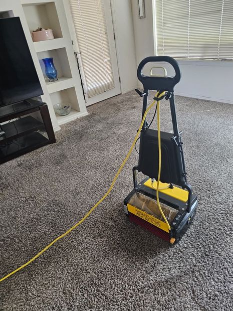 Yellow vacuum cleaner on a carpeted living room floor, with a cord trailing across the room.
