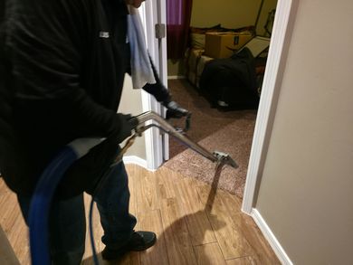 Person using a long-handled tool to clean a floor in a doorway, with a bucket nearby.