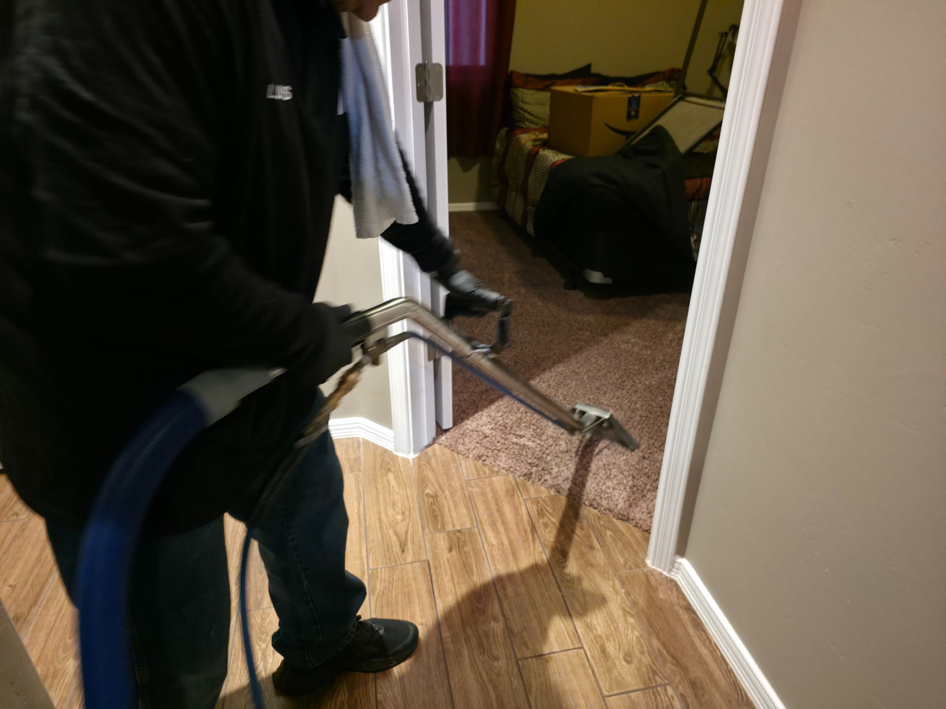 Person using a blue hose and spray wand to clean a hardwood floor indoors