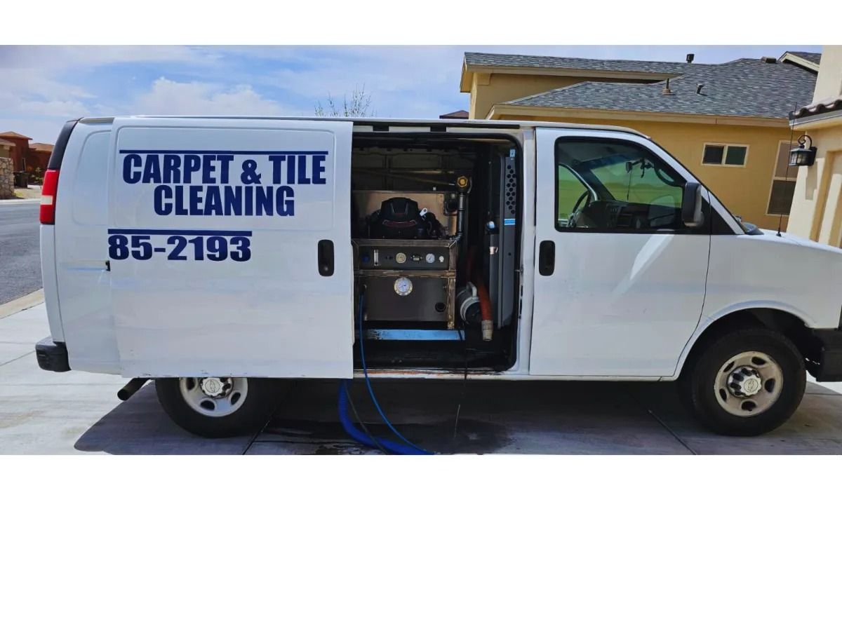 White carpet and tile cleaning van with side door open, showing equipment inside, parked outside a house.