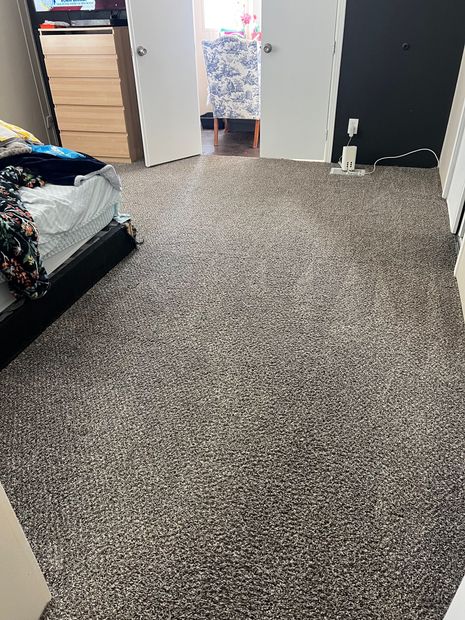 Carpeted bedroom with an open doorway, dresser, bed, and a person standing in the distance