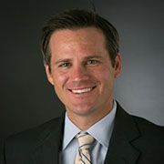 Smiling man in a dark suit and striped tie against a gray background