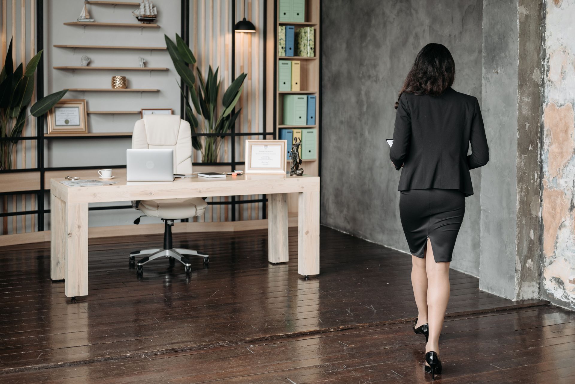 Person walking in a modern office with a white desk, plants, and stairs in the background