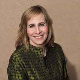 Smiling woman in a green patterned jacket against a beige wall
